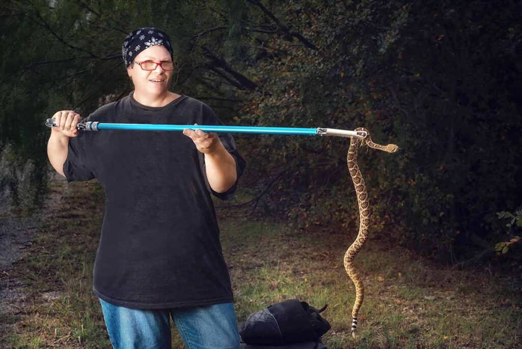 Miracle Bennett holds a western diamondback rattlesnake in a wooded area